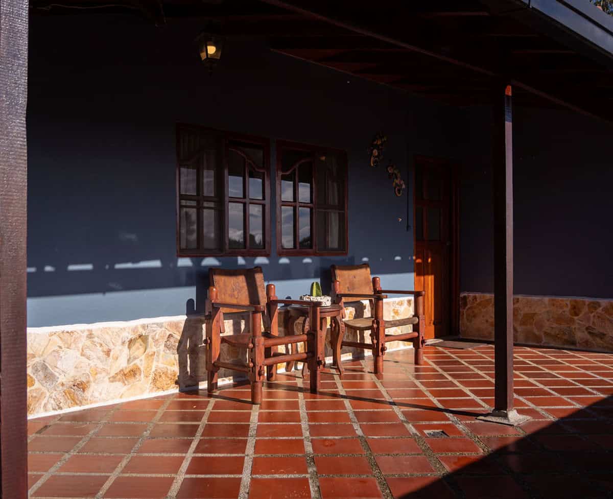 Home exterior with wooden chairs and terracotta tiled patio at Finca Conejo Blanco, rural retreat in Mexico.
