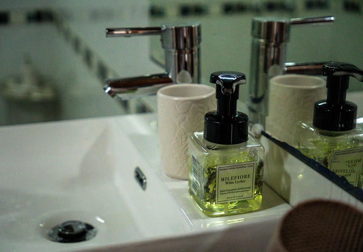 Hand soap dispenser with white ceramic mugs at CMS Finca Conejo Blanco, eco-friendly amenities for guests in a rustic setting.