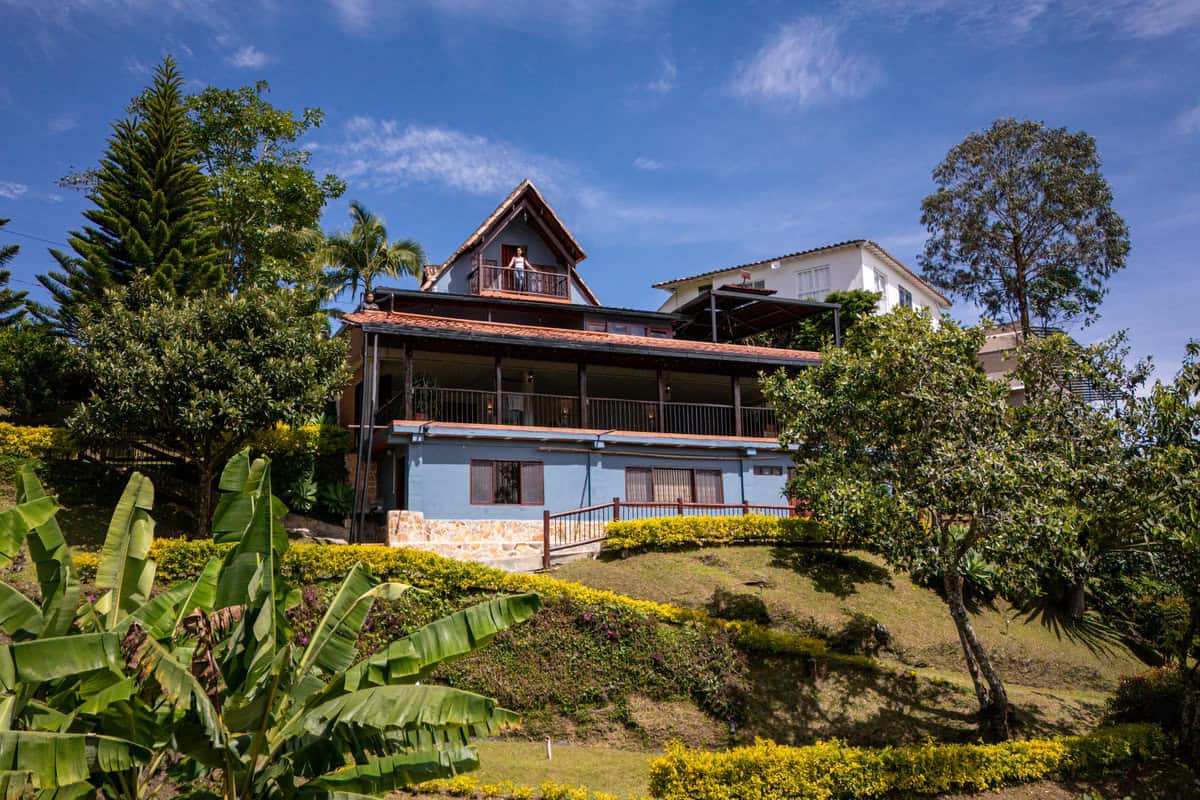 Charming blue house at Finca Conejo Blanco surrounded by lush greenery and vibrant garden landscape.